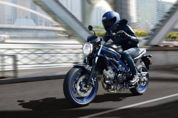 A rider on a Suzuki Sv650 motorcycle speeds along a city bridge in daylight, HD Desktop Wallpaper