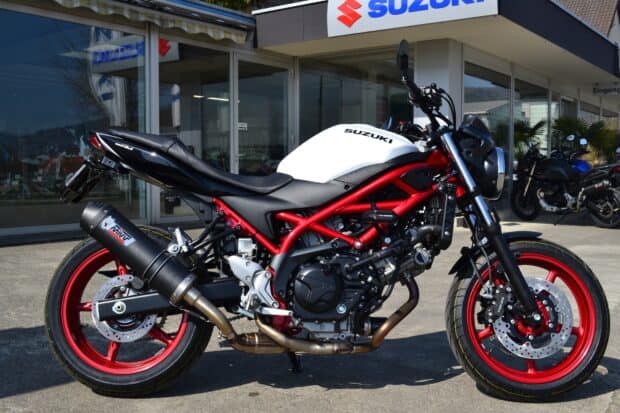 A Suzuki Sv650 motorcycle with a red frame parked outside a showroom, HD Desktop Wallpaper