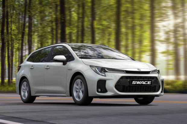 A white Suzuki Swace is shown driving past blurred trees on a forest road, HD Desktop Wallpaper