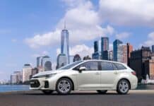 A white Suzuki Swace is parked near a city waterfront with skyscrapers in the background, HD Desktop Wallpaper