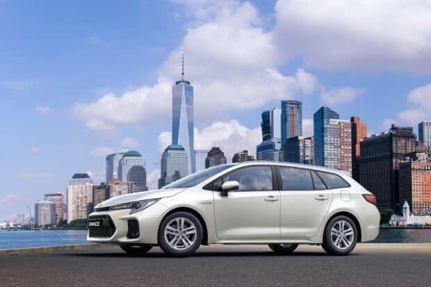 A white Suzuki Swace is parked near a city waterfront with skyscrapers in the background, HD Desktop Wallpaper