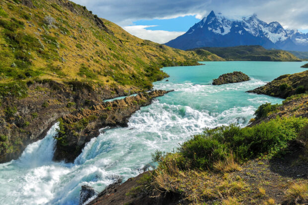 Lush green hills surrounding a turquoise river with a snow-capped mountain in the background, creating a stunning natural landscape in HD resolution.