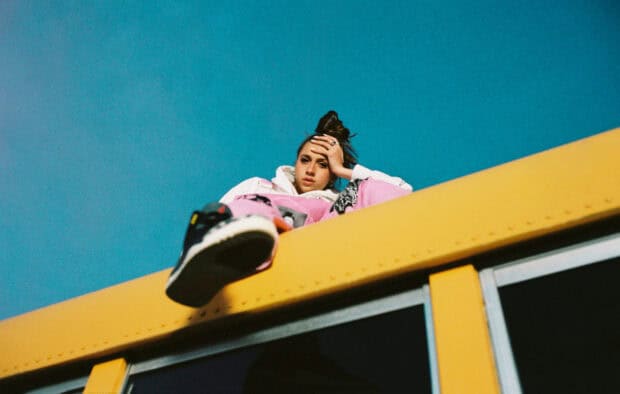 Tate Mcrae is sitting on a yellow bus looking relaxed on a clear blue sky day, HD Mobile Wallpaper