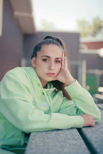Tate Mcrae Wallpapers features a young woman resting her head on her hand wearing a green hoodie, HD Phone Wallpaper