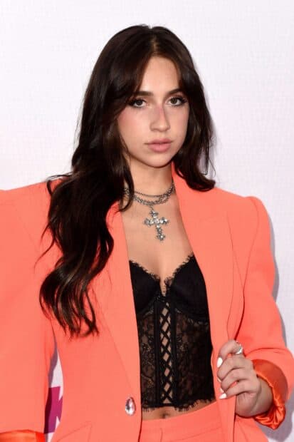 Tate Mcrae wears an orange suit with a black lace top and silver cross necklace, 2K Mobile Wallpaper