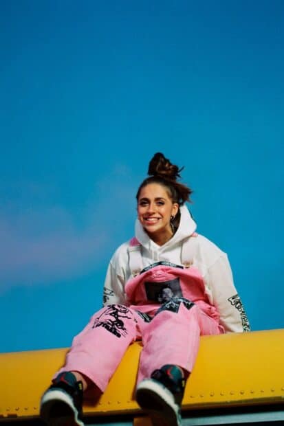 Tate Mcrae is smiling and sitting on a yellow surface wearing pink overalls, HD Phone Wallpaper