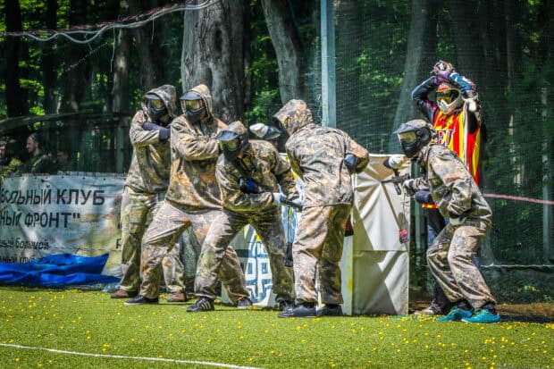 A group of players in camouflage gear ready for paintball with one player signaling, HD PC Wallpaper