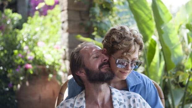 A tender moment between Tilda Swinton and a man in a lush garden setting, 2K Desktop Wallpaper