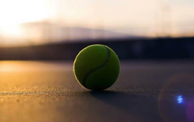 A tennis ball resting on the court surface with the sun setting in the background, 2K Desktop Wallpaper
