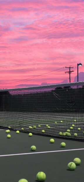 Tennis balls are scattered across the court under a pink sunset sky with a visible net, 2K Phone Wallpaper