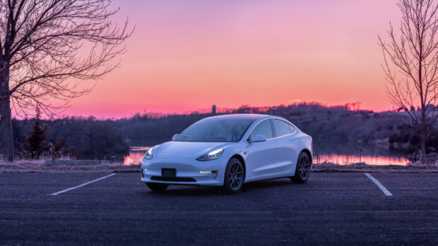 A white Tesla Model 3 is parked near a lake under a vibrant sunset sky, HD Desktop Wallpaper