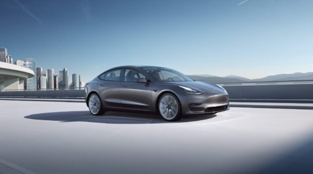 A Tesla Model 3 driving on a rooftop with city buildings in the background, 2K Desktop Wallpaper