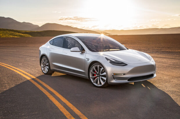 A silver Tesla Model 3 is parked on the road with mountains in the background during sunset, HD Desktop Wallpaper