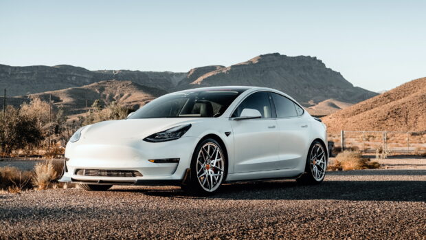 A white Tesla Model 3 parked on a deserted road with mountains in the background, 2K Desktop Wallpaper