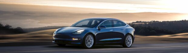 A Tesla Model 3 is driving along a road surrounded by hills and trees at sunset, 4K Desktop Wallpaper