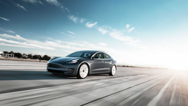 A Tesla Model 3 is driving fast on a wide open runway under a clear sky, HD Desktop Wallpaper