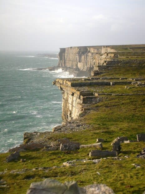 The Aran Islands show rocky cliffs and ocean waves under a cloudy sky, 2K Phone Wallpaper