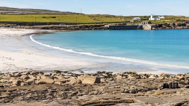 The Aran Islands show a peaceful blue sea with rock formations and distant houses, HD Desktop Wallpaper