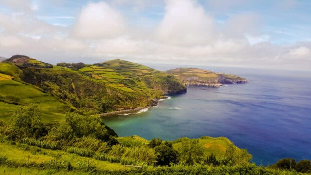 The Azores showcases lush green hills meeting the blue ocean under a cloudy sky, 2K Desktop Wallpaper