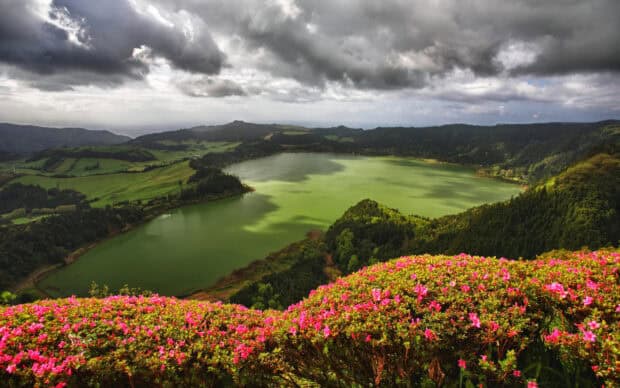 The Azores features a scenic lake surrounded by lush greenery and vibrant flowers under a cloudy sky, HD Desktop Wallpaper