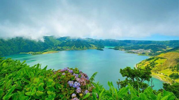 The Azores Wallpapers show a beautiful lake surrounded by green hills and colorful flowers under a cloudy sky, HD Desktop Wallpaper