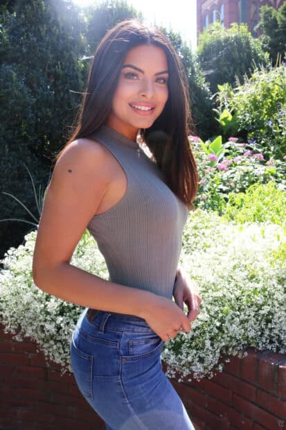 A smiling woman from The Bachelor Tv Series poses outdoors with greenery and flowers behind her, HD Mobile Wallpaper