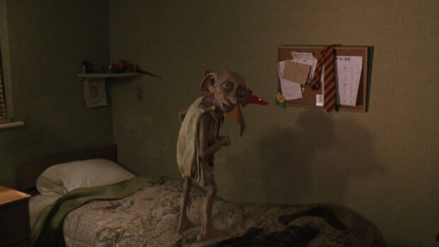 A house elf stands on a bed in a dimly lit room with a noticeboard behind, HD Desktop Wallpaper