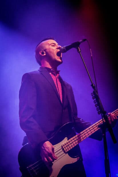 The Interrupters lead singer passionately sings while playing bass guitar on stage, HD Mobile Wallpaper