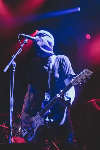 A masked musician from The Interrupters plays guitar on stage under colorful lights, HD Mobile Wallpaper