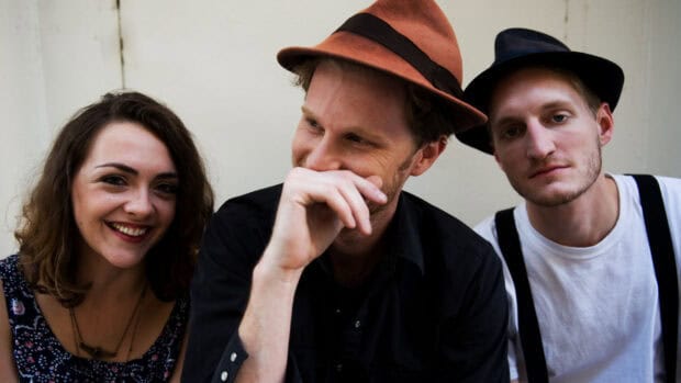 The Lumineers show three members sitting together with relaxed expressions and casual hats, HD Desktop Wallpaper