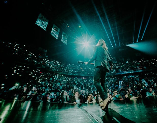 The Lumineers perform on stage with a guitar in front of a large cheering audience, HD Desktop Wallpaper