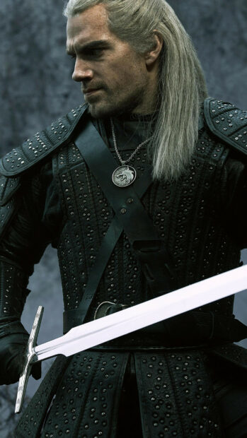 A man with long hair wearing detailed armor holds a sword in The Witcher Tv Series wallpapers, 2K Mobile Wallpaper