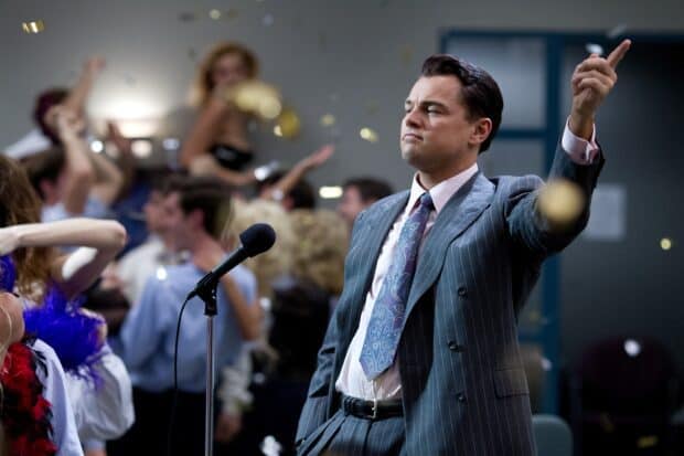 A man in a suit confidently gestures at a lively party with people dancing and celebrating, 2K Desktop Wallpaper