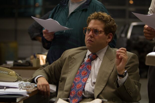 A man in a suit and glasses appears focused while sitting at a cluttered desk in an office, HD Desktop Wallpaper