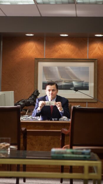 A man in a suit holding a dollar bill sitting in an office setting with a painting of a sailboat, HD Mobile Wallpaper