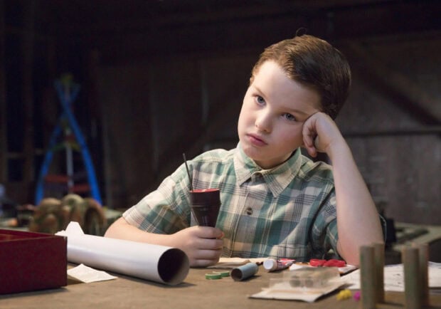 A young boy sitting at a wooden table holding a small device, Young Sheldon Tv Series Wallpapers, 2K Desktop Wallpaper