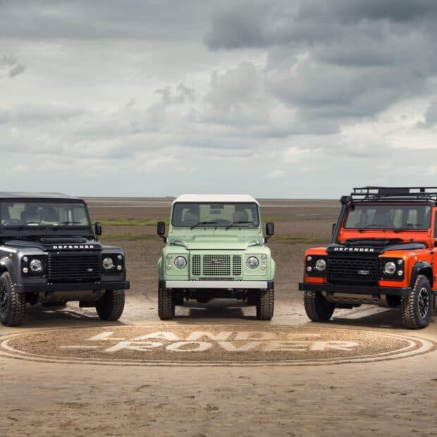 Three Land Rover Defender models with different colors lined up on a sandy beach under a cloudy sky, HD Desktop Wallpaper