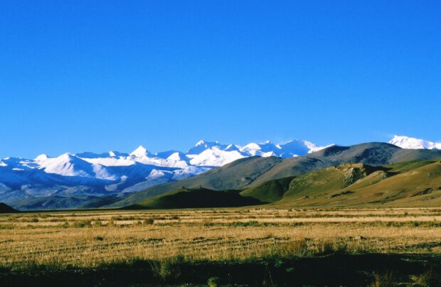A panoramic view of the Tibetan highlands with snow capped peaks under a clear blue sky, 2K Desktop Wallpaper
