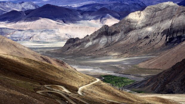 A winding road passes through the Tibetan Highlands scenic mountain range with rocky peaks and green valley, 4K Desktop Wallpaper