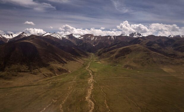 A vast landscape of Tibetan Highlands with snow capped mountains and green valleys under a cloudy sky, HD Desktop Wallpaper