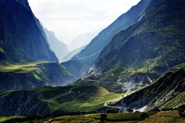 A winding road cuts through the lush green Tibetan highlands valley with mountains surrounding it, 2K Desktop Wallpaper