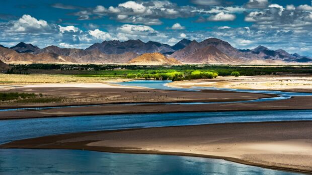 The Tibetan highlands feature a winding river surrounded by mountains and green vegetation, HD Desktop Wallpaper