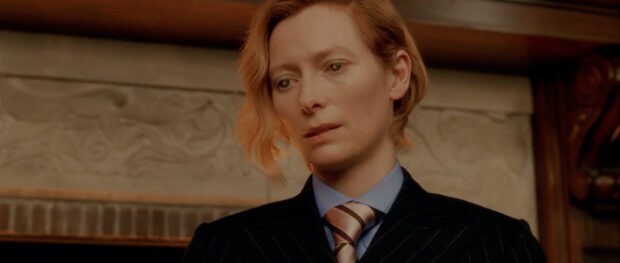 Tilda Swinton looks thoughtfully ahead wearing a striped tie and suit, 2K Desktop Wallpaper