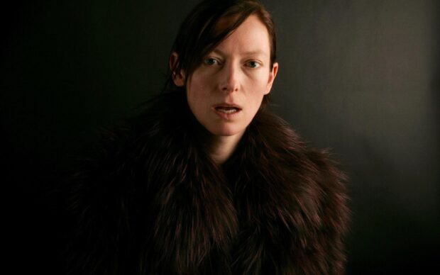 Tilda Swinton wears a dark fur coat with a serious expression against a black background, HD Desktop Wallpaper