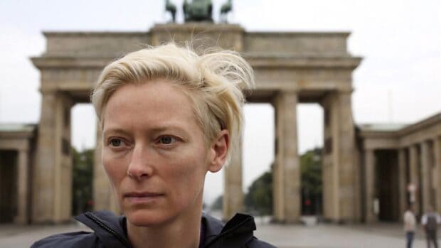 Tilda Swinton looks thoughtfully with the Brandenburg Gate blurred in the background, HD Desktop Wallpaper