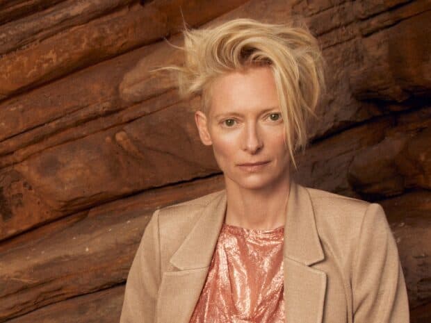 A close up of Tilda Swinton wearing a beige jacket and shiny top by orange rocks, HD Desktop Wallpaper