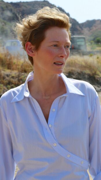 Tilda Swinton wears a light striped shirt standing outside near dry grass and hills, HD Mobile Wallpaper
