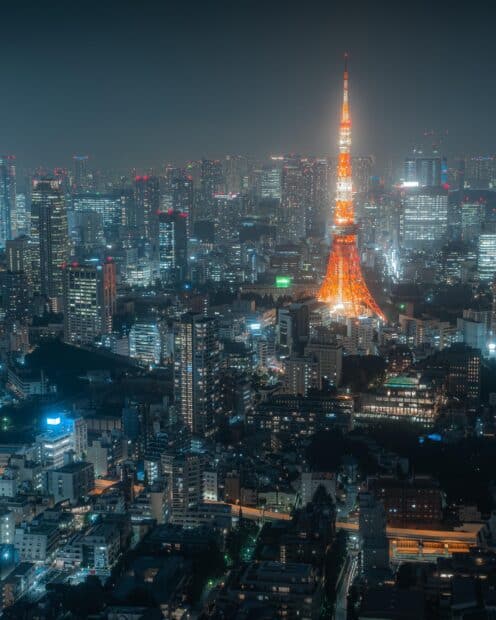 Tokyo Tower glowing brightly over a city at night with surrounding buildings, 2K Desktop Wallpaper