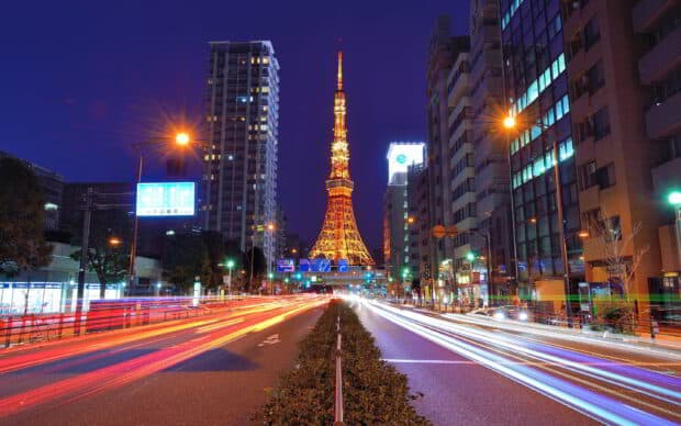 The Tokyo Tower illuminated at night with light trails from passing cars on the busy city street, 2K Desktop Wallpaper