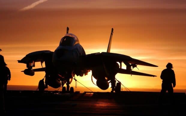 A Top Gun Maverick jet is parked on a carrier deck during sunset with crew members nearby, HD Desktop Wallpaper